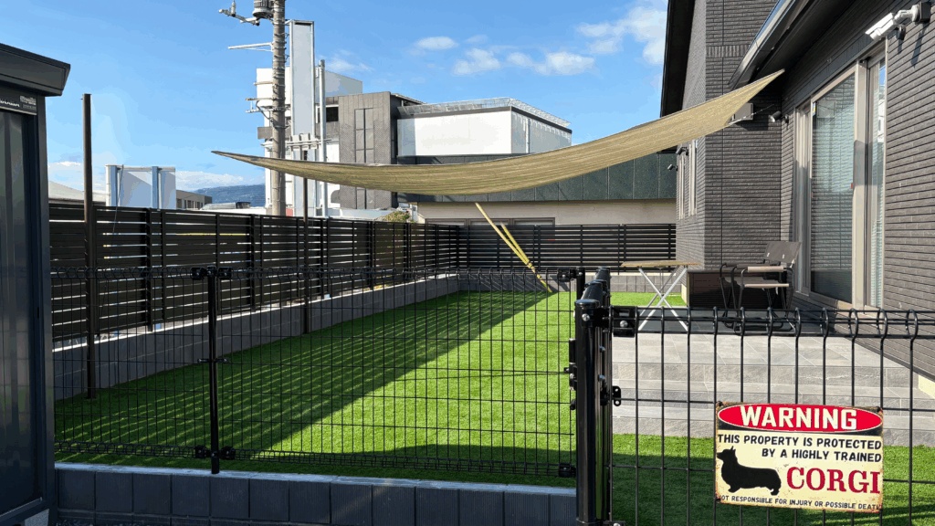 M様邸の新築外構は、 ブラックとグレーをベースにした統一感のあるデザインが特徴です。 木目調の部分も、あえて暗めの色を選び、 建物とよくなじむ落ち着いた印象に仕上げました。 お庭には、35mmのふかふか人工芝を使用。 ワンちゃんが走っても足にやさしく、 広々としたドッグランとして楽しめます。 門扉やフェンスは、角を丸くした形を選び、 すき間や高さにも気を配りました。 ブロックを含めて約1.6mの目隠しフェンスで、 外からの視線もしっかりカットしています。 また、 上げ下げできるシェード 人感センサー付きライト 落とし棒を2本付けた動きにくい門扉 など、 ワンちゃんもご家族も安心できる工夫をたくさん取り入れました。