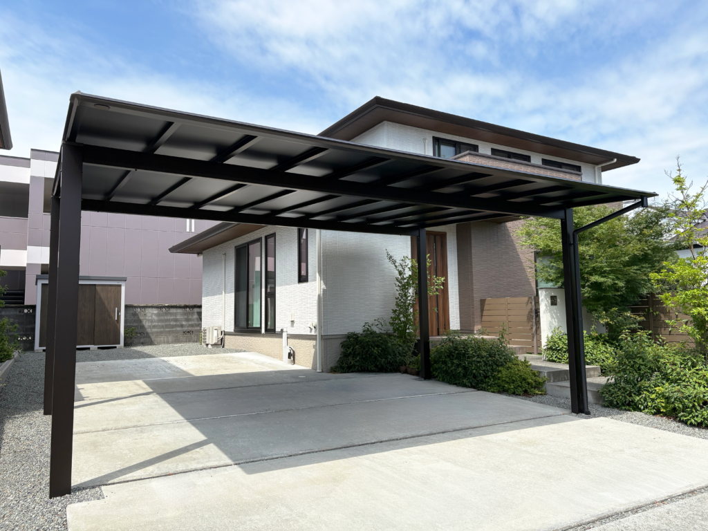 富士宮市で施工した三協アルミ・スカイリード2台用カーポート。ブラックポリカ屋根を採用し、建物や植栽と調和する外構に仕上げた施工事例。